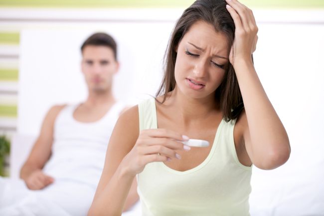 Upset woman looking in pregnancy test with her husband in background