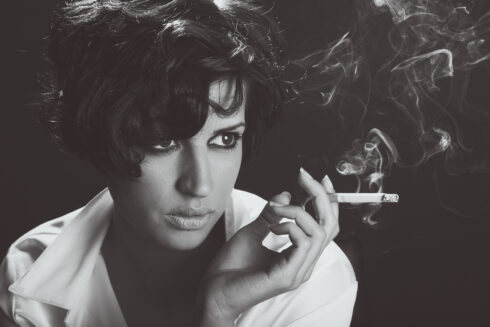 Close-up portrait of a brunette woman smoking a cigarette on black background