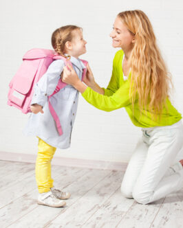 Mother helps her daughter get ready for school. Mom support child to wear a backpack