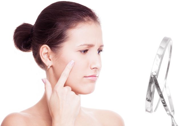 young woman having skin porblems, looking into the mirror isolated against white background