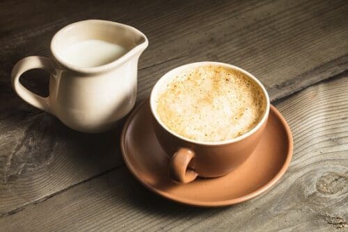 Coffee in brown cup and milk jug on tha table