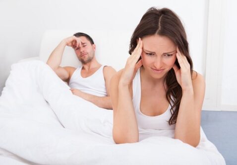 Frustrated Woman Sitting On Bed In Front Of Young Man