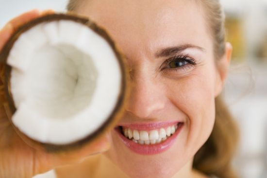 Happy young woman holding coconut piece in front of eye