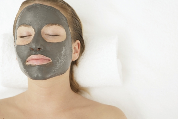 Young woman with a facial mud mask lying on a divan bed, close-up