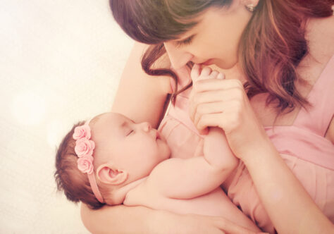 caring mother kissing little fingers of her cute sleeping baby girl, happy family concept