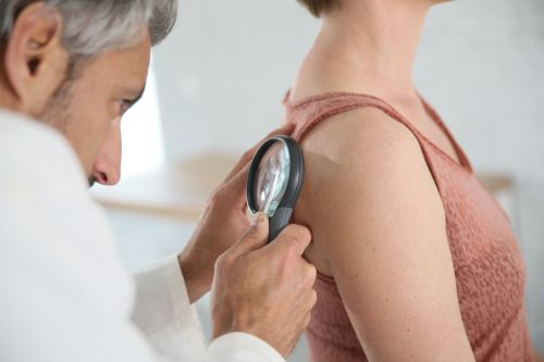 Dermatologist looking at woman's mole with magnifier
