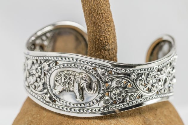 Old silver Bangle, elephant pattern Thai style, set on mahogany seed background.