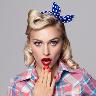 Portrait of beautiful young surprised woman, dressed in pin-up style. Caucasian blond model posing in retro fashion and vintage concept studio shoot, on grey background.