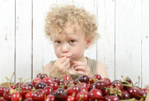 a little blond boy playing with cherries