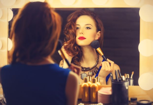 Portrait of a beautiful woman as applying makeup near a mirror. Photo in retro color style.