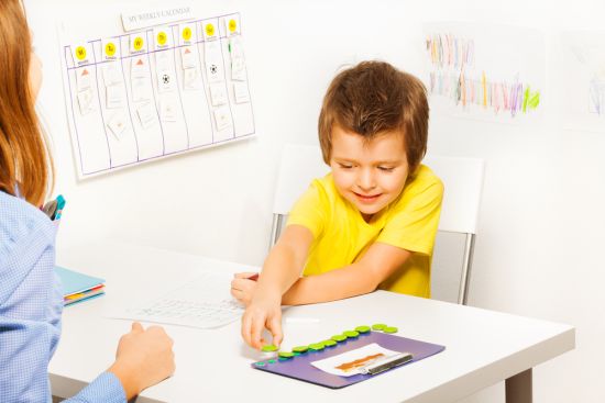 Smiling boy puts coins during developing game with his parent sitting opposite at the table in the room
