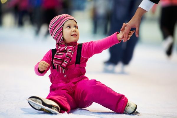 Mother’s hand help little cute girl on the rink
