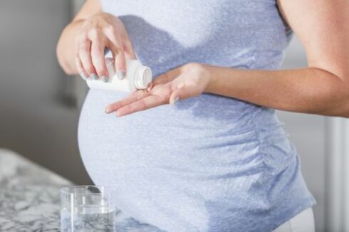 Cropped view of pregnant woman taking pill with glass of water, possibly a prenatal vitamin.
