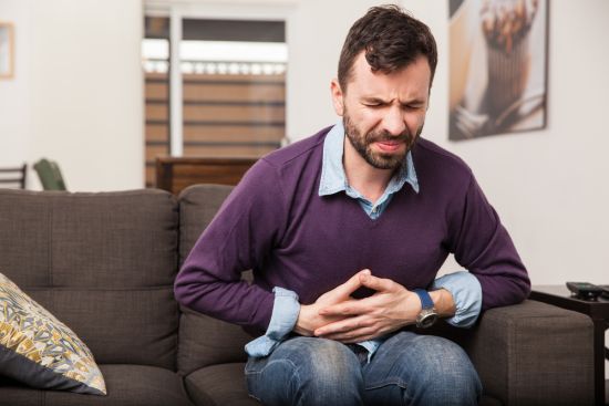 Guy with a beard feeling unwell with a stomach ache while sitting in a couch at home