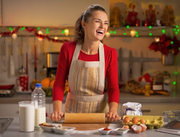 Smiling young housewife making dough in christmas decorated kitchen