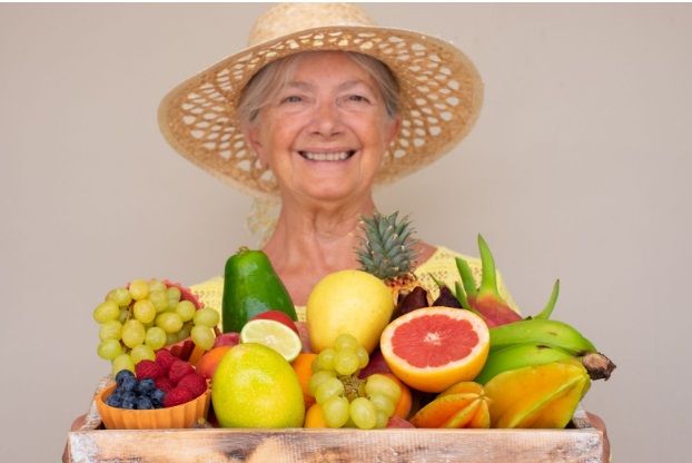 uśmiechnięta seniorka trzymająca skrzynkę z owocami
